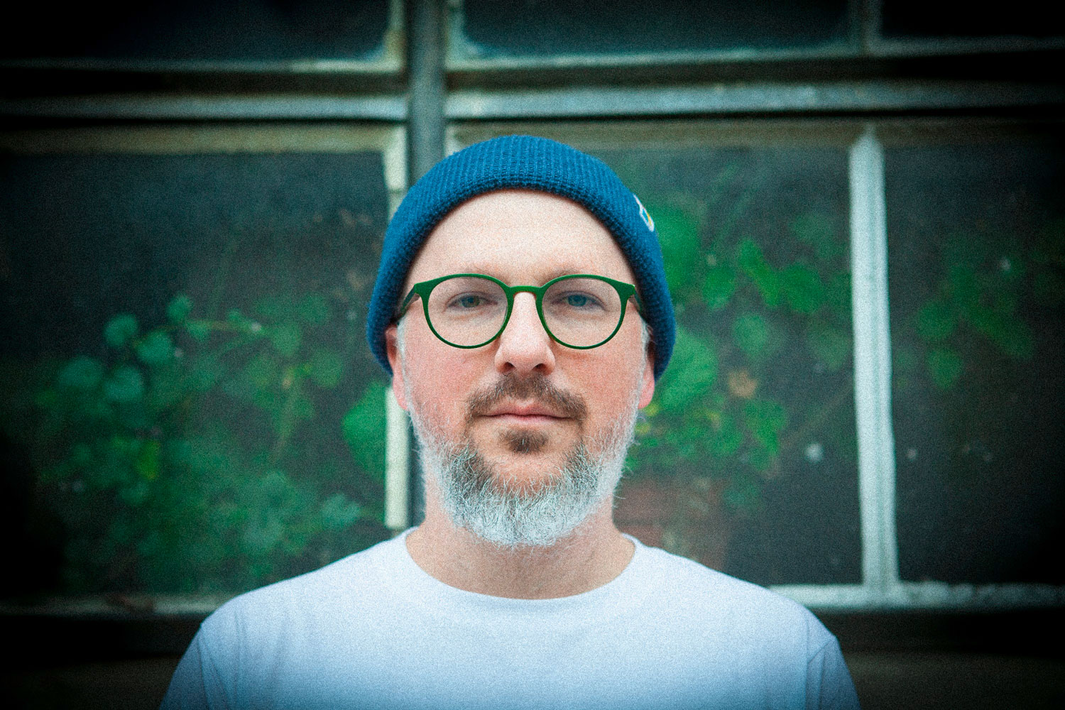 Porträtfoto von Johannes Ludwig mit Bart, blauer Mütze und grüner Brille blickt er frontal in die Kamera