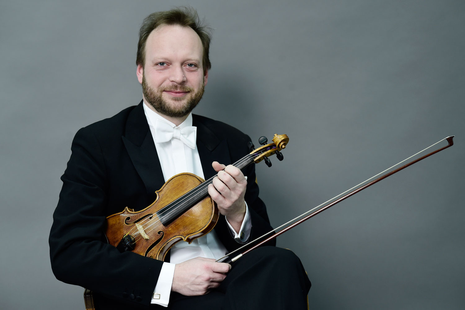 Ein Mann mit schwarzem Anzug, weißem Hemd und weißer Fliege blickt, mit seiner Violine unterm Arm, freundlich in Richtung Kamera